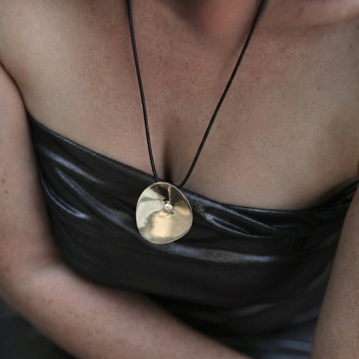 Sculptural Cirque pendant in bronze with freshwater pearl, suspended on black leather cord with sterling silver teardrop accents, worn long or tied as a bold modern necklace.