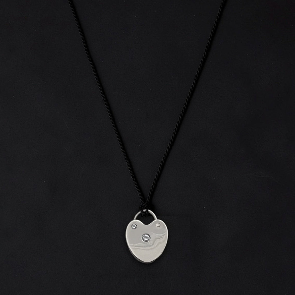Sculptural Sterling silver heart lock pendant with bezel-set diamonds, suspended from an adjustable black cord necklace.