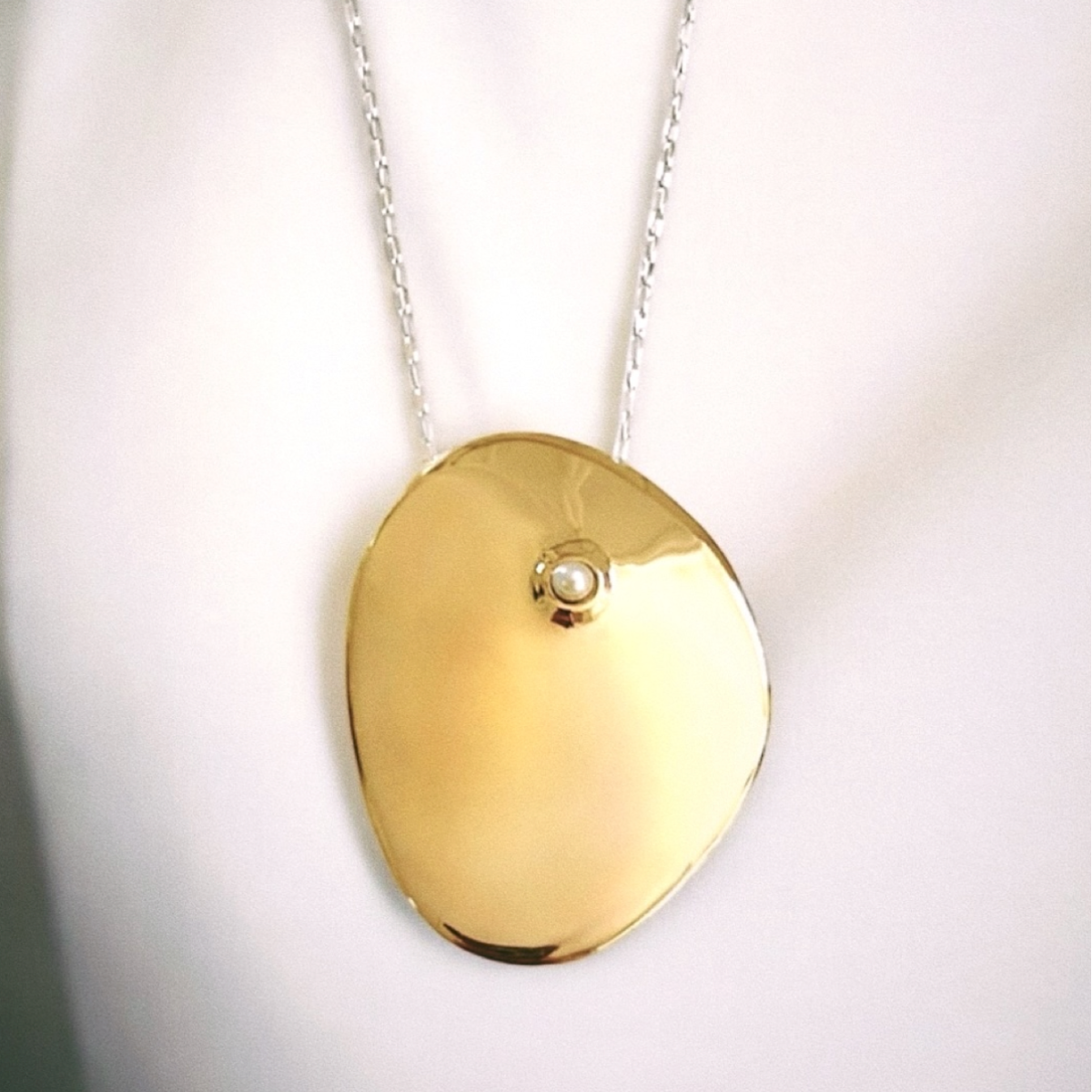 An asymmetrical gold pendant necklace inspired by nature and embellished with a freshwater pearl and gold box chain.