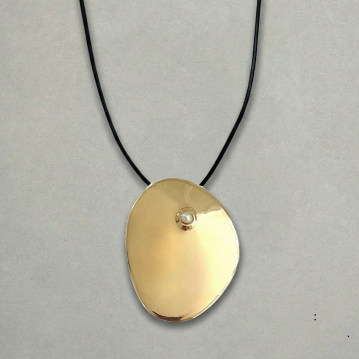 Cirque cord pendant necklace with freshwater pearl, finished with sterling silver teardrop accents. Sculptural bronze pendant worn as a long 32-inch strand or tied as a bold statement necklace.