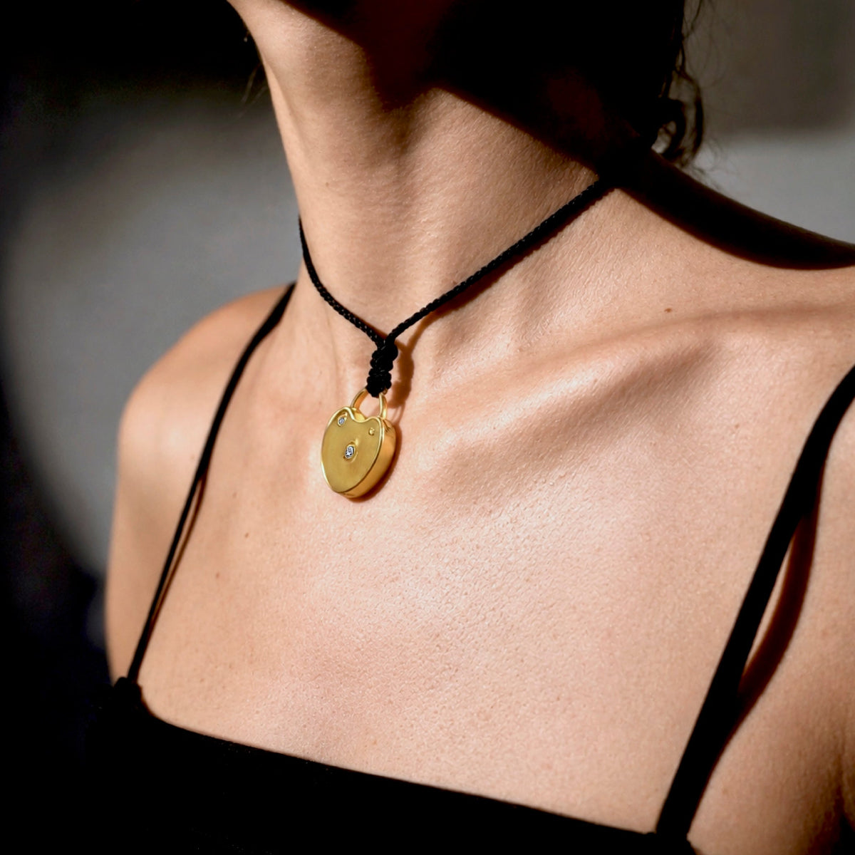Sculptural gold-plated heart lock pendant with bezel-set diamonds on an adjustable black cord necklace, styled on model. Jacqueline Rose Collection luxury jewelry.