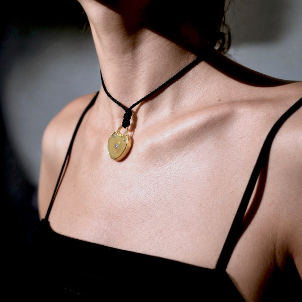 Sculptural gold-plated heart lock pendant with bezel-set diamonds on an adjustable black cord necklace, styled on model. Jacqueline Rose Collection luxury jewelry.